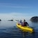 2 people in a 2 seat kayak paddling on a lake surrounded by verdant land masses
